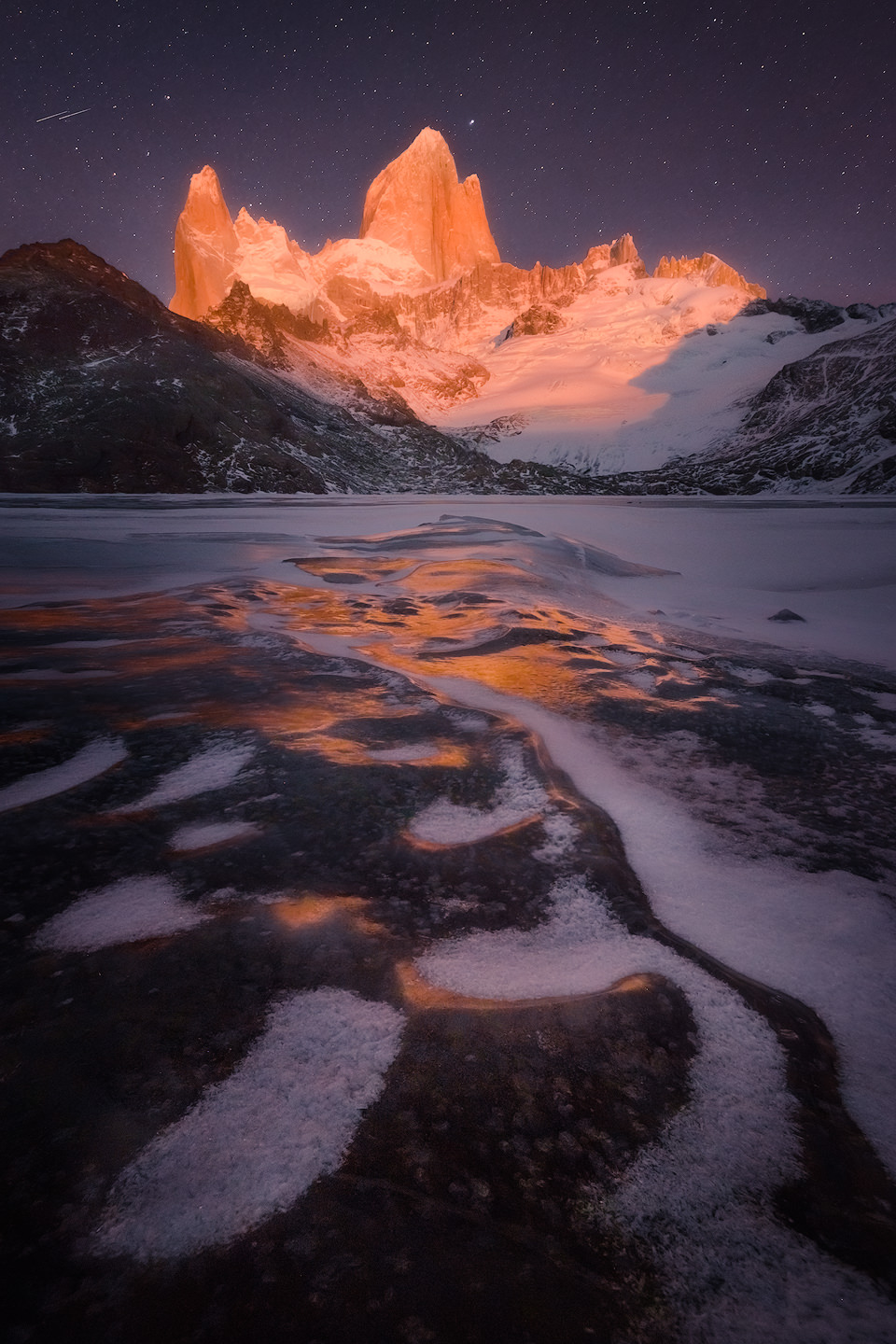Fitz Roy glowing red during a winter moonrise behind frozen Laguna de los Tres .